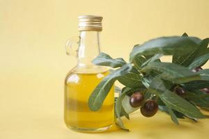 Flasche Olivenöl und frisches Olivenblatt auf gelbem Hintergrund foto