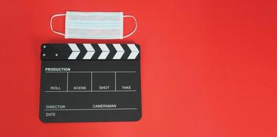 schwarze Klappe oder Filmtafel mit Gesichtsmaske. es wird in der videoproduktion, in der film- und kinoindustrie auf rotem hintergrund verwendet. foto