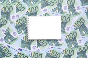 weißes notizbuch mit sauberen seiten, die auf einer reihe grüner geldstückelungen von 100 euro liegen. viel Geld bildet einen unendlichen Haufen foto