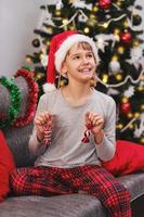 süßes lustiges baby in einem weihnachtsmann-hut mit weihnachtsschmuck an den ohren und in den händen foto