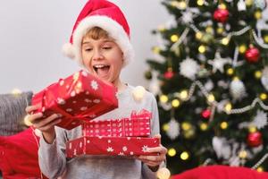 porträt eines glücklichen kindes, das am weihnachtsmorgen geschenke in der nähe des weihnachtsbaums hält foto