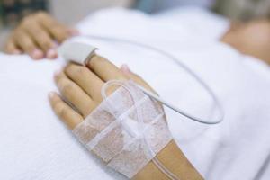 Nahaufnahme Menschen konzentrieren sich auf die Hand eines kranken Patienten auf dem Bett in der Krankenstation. Gesundheitswesen und Medizin. Linie Kochsalzlösung und Pulsdetektor Blutsauerstoffmessgerät am Finger der Menschen. foto