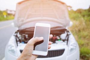 kaputtes auto auf der straße und smartphone, frauenhand, die mobiles smartphone hält, handykontakt bitten um hilfe autotechniker reparieren das auto in der garage. foto