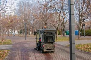 Der kommunale Dienst führt saisonale Arbeiten im Park durch. Die Kehrmaschine nimmt viel Schmutz auf. die Bürsten fegen den Asphalt foto