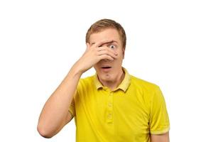 ängstlicher junger Kerl, der durch die Finger im gelben Polo-T-Shirt schaut, weißer isolierter Hintergrund foto