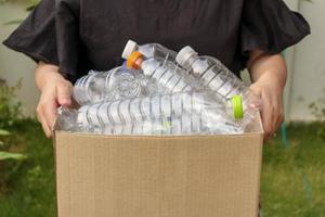 Hand, die eine braune Recycling-Müllbox mit Plastikflaschen hält foto