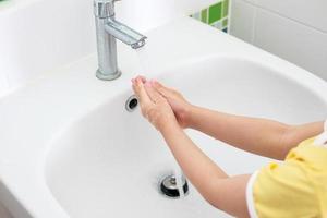 kleines Mädchen wäscht sich die Hand unter dem Wasserhahn mit Wasser foto