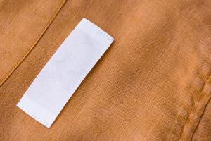 weißes, leeres Kleidungsetikett auf braunem Leinenstoff-Texturhintergrund foto