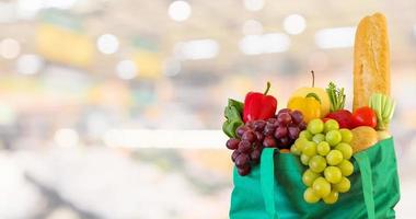 frisches obst und gemüse in wiederverwendbarer grüner einkaufstasche mit supermarkt-lebensmittelgeschäft verschwommener defokussierter hintergrund mit bokeh-licht foto