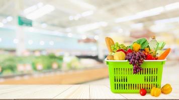 einkaufskorb gefüllt mit obst und gemüse auf holztisch mit supermarkt-lebensmittelgeschäft verschwommener defokussierter hintergrund mit bokeh-licht foto