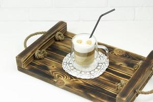 ein glas kaffee cappuccino steht auf einem holztablett foto