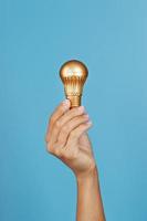 goldene glühbirne in der hand auf blauem hintergrund, als konzept für ideen und unterstützung