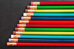Mehrfarbige Bleistifte zum Zeichnen und Zeichnen in einer Reihe auf einem strukturierten schwarzen Hintergrund in einer Reihe foto