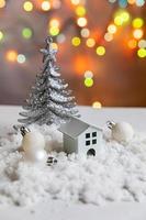 abstrakter Adventsweihnachtshintergrund. Spielzeugmodellhaus und Winterdekorationen Ornamente auf dem Hintergrund mit Schnee und defokussierten Girlandenlichtern. weihnachten mit familienkonzept zu hause. foto