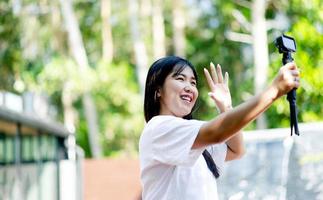 asiatisches mädchen schön, breit lächelnd, zu hause stehend und ein leichtes selfie genießend. mit einer Kompaktkamera auf einem unscharfen Hintergrund foto