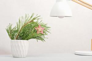 Kieferzweig in weißer Vase auf Tischplatte neben Schreibtischlampe. minimale weihnachtliche wohnkultur, winterurlaub bürodekor. Platz kopieren. foto