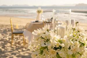 Schöner Tisch für ein romantisches Abendessen am Strand mit Blumen und Kerzen. Catering für ein romantisches Date, eine Hochzeit oder einen Flitterwochenhintergrund. Abendessen am Strand bei Sonnenuntergang. ausgewählten Fokus. foto