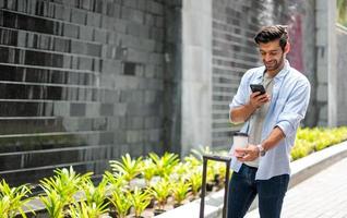 junger kaukasier, der telefon hält und foto von kaffeetasse, tasche und spaziergang in der stadtstraße macht.