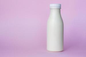 eine Flasche weiße Milch, hervorgehoben auf einem rosa Hintergrund, Nahaufnahme. foto