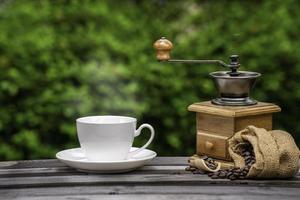 Kaffeetasse mit Mühle, dunkle Kaffeebohnen auf dem alten Holzboden, Nahaufnahme von Kaffeesamen auf natürlichem Hintergrund. foto
