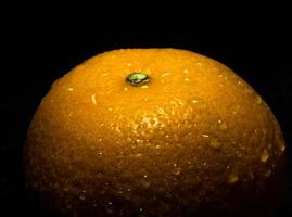 Wassertropfen auf glänzender Oberfläche von Frische Orange auf schwarzem Hintergrund foto