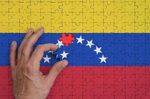 Die venezolanische Flagge ist auf einem Puzzle abgebildet, das die Hand des Mannes zum Falten vervollständigt foto