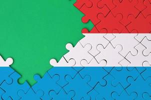 Die luxemburgische Flagge ist auf einem fertigen Puzzle mit freiem Platz für grüne Kopien auf der linken Seite abgebildet foto