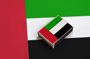 Die Flagge der Vereinigten Arabischen Emirate ist auf einer Streichholzschachtel abgebildet, die auf einer großen Flagge liegt foto