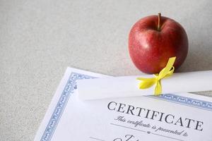 Auf dem Tisch liegt ein Leistungszertifikat mit kleiner Schriftrolle und rotem Apfel. Bildungsunterlagen foto