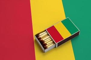 Die guinea-Flagge wird in einer offenen Streichholzschachtel gezeigt, die mit Streichhölzern gefüllt ist und auf einer großen Flagge liegt foto