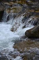 Nahaufnahme eines kleinen wilden Wasserfalls in Form von kurzen Wasserströmen zwischen Bergsteinen foto