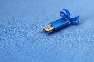 Eine leuchtend blaue USB-Flash-Speicherkarte mit einer blauen Schleife liegt auf einer Decke aus weichem und pelzigem hellblauem Fleece-Stoff. klassisches weibliches Geschenkdesign für eine Speicherkarte foto