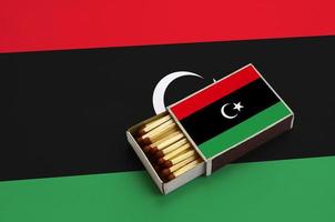 Die libysche Flagge wird in einer offenen Streichholzschachtel gezeigt, die mit Streichhölzern gefüllt ist und auf einer großen Flagge liegt foto
