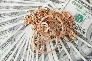 Viele teure goldene Schmuckringe, Ohrringe und Halsketten auf einer großen Menge von US-Dollar-Scheinen aus nächster Nähe. Pfandhaus oder Juweliergeschäft foto