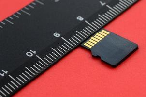 kleine micro sd-speicherkarte liegen auf rotem hintergrund neben einem schwarzen lineal. ein kleiner und kompakter Daten- und Informationsspeicher foto