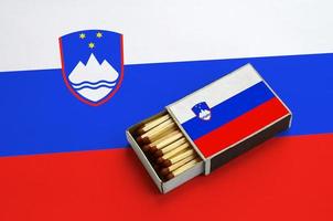 Die slowenische Flagge wird in einer offenen Streichholzschachtel gezeigt, die mit Streichhölzern gefüllt ist und auf einer großen Flagge liegt foto