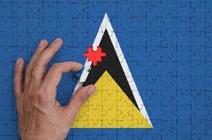 die flagge von st. lucia ist auf einem puzzle abgebildet, das die hand des mannes zum falten vervollständigt foto