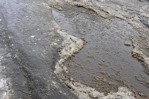 Beschädigte Asphaltstraße mit Schlaglöchern, die durch Frost- und Tauzyklen im Winter verursacht wurden. schlechte Straße foto