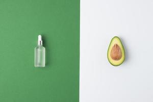 minimale komposition mit kosmetikflasche und avocado auf grün-weißem hintergrund. flach liegend, kopierraum foto