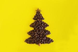 winterkomposition mit weihnachtsbaum aus kaffeebohnen und verziertem anisstern und zimtstange auf gelbem hintergrund, flach gelegt. grußkarte für das neue jahr mit kopienraum. foto