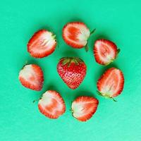 Ein Kreis aus Erdbeerhälften und ganzen Erdbeeren in einer Mitte auf einem helltürkisfarbenen Hintergrund, Draufsicht. Gesundes Sommeressen. foto