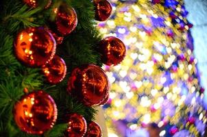 rote Kugelverzierung, die am Weihnachtsbaum mit buntem Bokeh-Hintergrund in Herzform von einem anderen für Weihnachtsferien hängt foto
