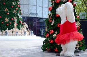 teddybär trägt rotes kleid, das neben weihnachtsbaum für weihnachtsfeiertagsdekoration steht. foto