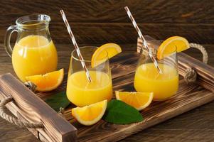 Frischer Orangensaft in Gläsern mit geschnittenen Orangen auf Holztablett. rustikales Stillleben mit Zitrusfrüchten foto