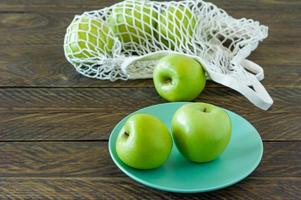 Bio-Oma-Smith-Äpfel auf einem Teller mit Mesh-Textiltasche auf Holztisch.