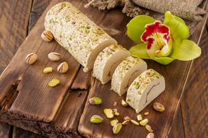 in Scheiben geschnittene Tahini Halva mit Pistazien auf einem mit Blumen geschmückten Holztisch foto