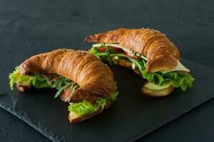 Croissant-Sandwiches mit gesalzenem Lachs auf einem Schreibtisch, serviert mit frischen Salatblättern, Rucola und Gemüse auf schwarzem Hintergrund foto