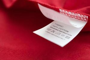 Weiße Wäschepflege Waschanleitung Kleideretikett auf rotem Baumwollhemd foto