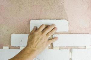 Die Hand des Meisters legt dekorative Fliesen unter den Ziegel an der Wand. das Ende der modernen Ausbauarbeiten. foto