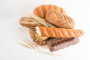 Eine Auswahl an gebackenem Brot aus verschiedenen Mehlen auf einem Holzbrett und einem weißen Hintergrund mit Ohren aus Weizen und Flachs und Sesam. foto